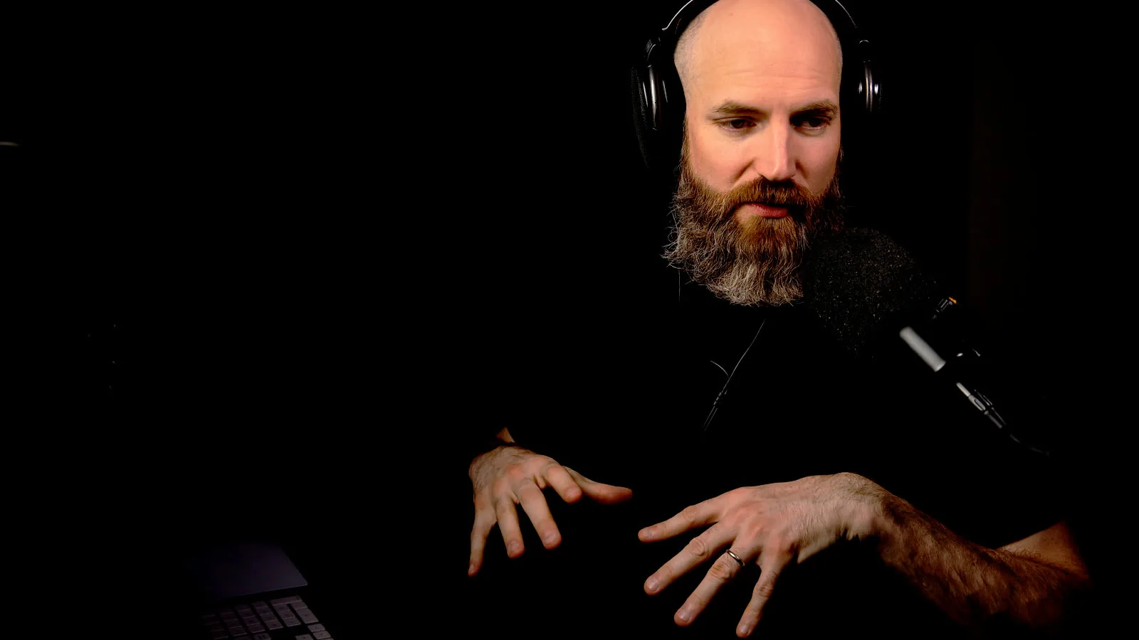David Glenn at the desk in headphones, both hands over the keyboard mid-explanation